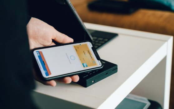 Eine Person, die ein Smartphone über einen Kartenleser hält, um kontaktlos zu bezahlen