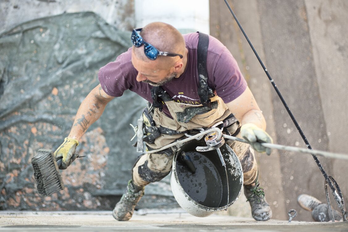 Bild von Damir Mijailovic auf Pexels:  Handwerker trägt Kalkputz auf eine historische Hausfassade auf, daneben liegen Farbmuster