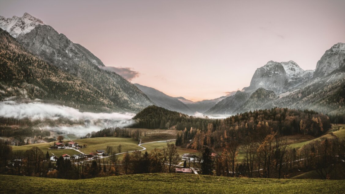Bild von Felix Mittermeier auf Pexels: Alpendorf im Winter bei Sonnenaufgang, umgeben von nebeligen Bergen und dichten Wäldern