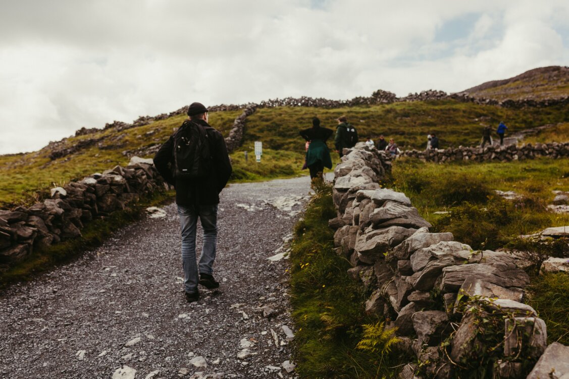 Bild von Jonathan Borba auf Pexels: Reisende gehen auf einem historischen Steinpfad auf Inishmore durch üppiges Grün
