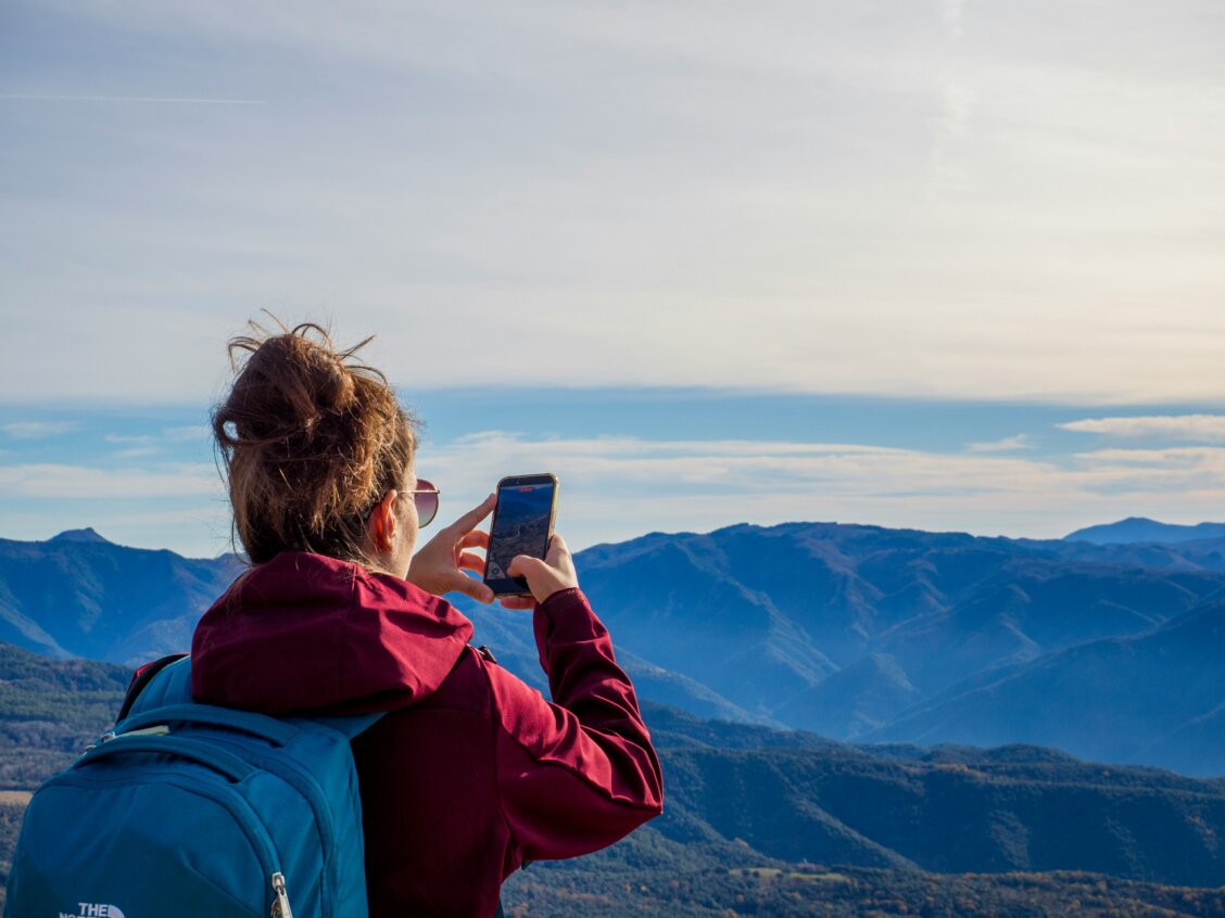 Bild von Sergi Kabrera auf unsplash: Frau, die mit dem Handy ein Foto von Bergen macht